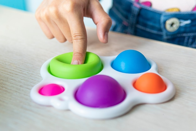 Foto una ragazza divertente si nasconde dietro un giocattolo. ritratto bambina con un moderno giocattolo popit. colorato e luminoso giocattolo pop-it semplice fossetta. gioco sensoriale antistress fidget push semplice fossetta