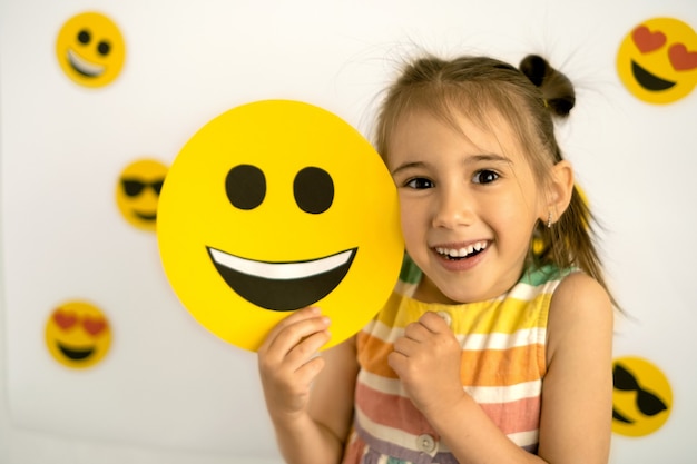 a funny girl is holding a happy emoji emoticon in her hands world smile day