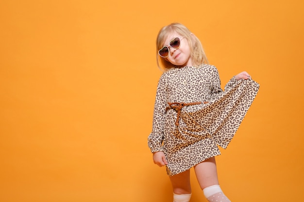 Funny girl in leopard dress and glasses on yellow background posing