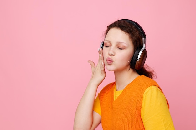 Funny girl listening to music with headphones orange sweater emotions fun pink background unaltered