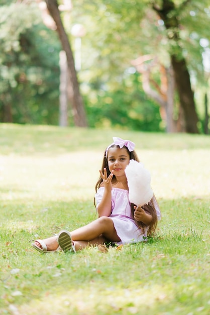 Funny girl in pink dress eats cotton candy in summer in the park