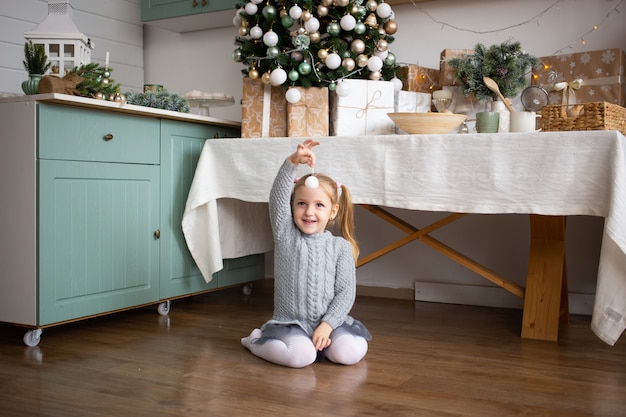 面白い女の子がキッチンでクリスマスツリーのおもちゃで遊ぶ