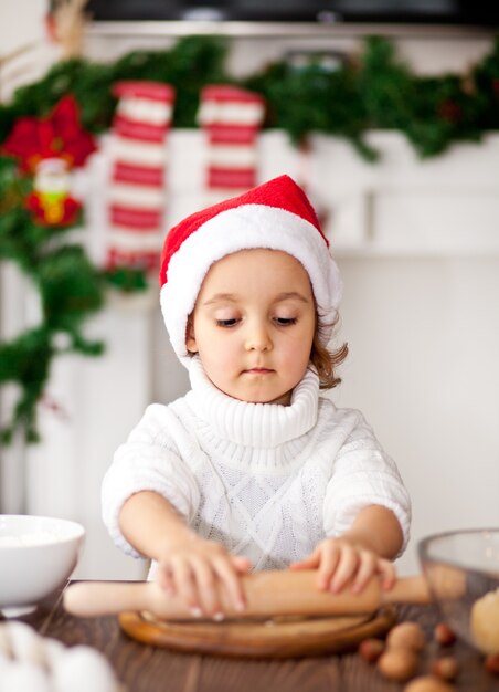 家でクリスマスのクッキーを焼くサンタの帽子の面白い女の子。