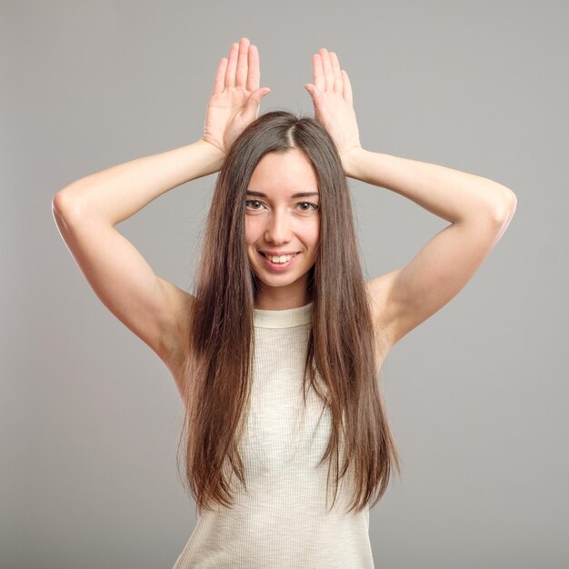 Funny girl showing bunny ears with her hands isolated on gray background