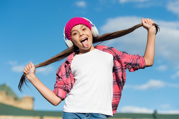 Funny girl stick out tongue listening to music and holding long brunette hair sunny sky, haircare.