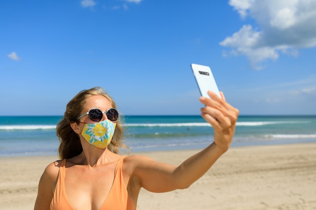 Funny girl taking selfie photo by smartphone on tropical sea beach.