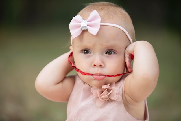 Photo the funny girl took a red ribbon in her mouth one year old child a cute baby