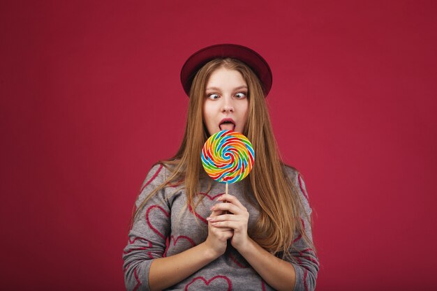 Funny girl wearing hat eating big striped lollipop