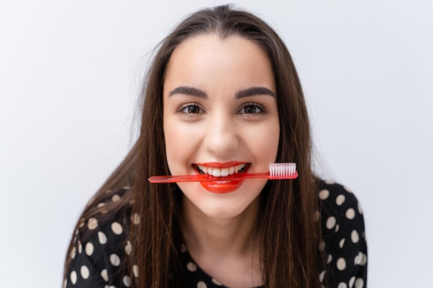 Funny girl with red lips keeps toothbrush between healthy white teeth. White background. Oral care concept.