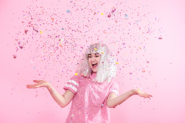 Смешная девчонка с серебряными волосами дарит улыбку и эмоции на розовой стене. молодая женщина или девушка с конфетти