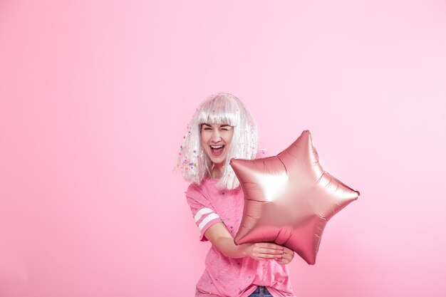 Funny Girl with silver hair gives a smile and emotion on pink wall. Young woman or teen girl with balloons and confetti