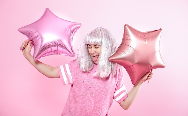 Funny Girl with silver hair gives a smile and emotion on pink wall. Young woman or teen girl with balloons and confetti