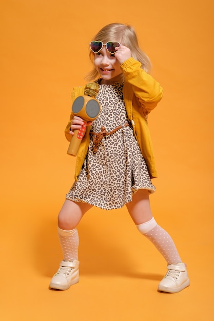 Funny girl in yellow clothes on yellow background with microphone in hand