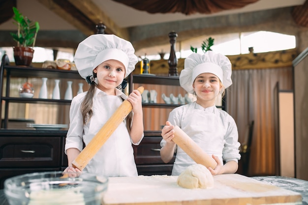 Funny girls kids are preparing the dough in the kitchen.