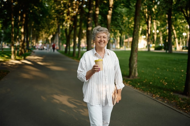 Funny granny drinks coffee in summer park