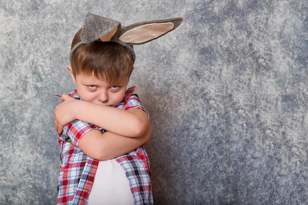 Photo a funny grumpy little boy dressed in a red checkered shirt has a rabbit ears on his head