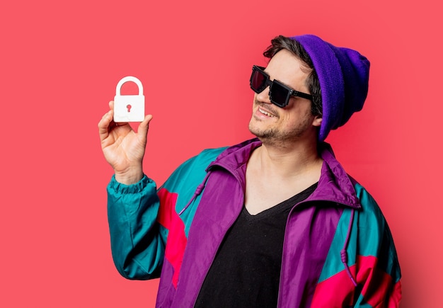 80 년대 스타일의 재킷과 선글라스에 재미있는 사람이 빨간색 backgorund에 자물쇠 기호를 붙입니다.