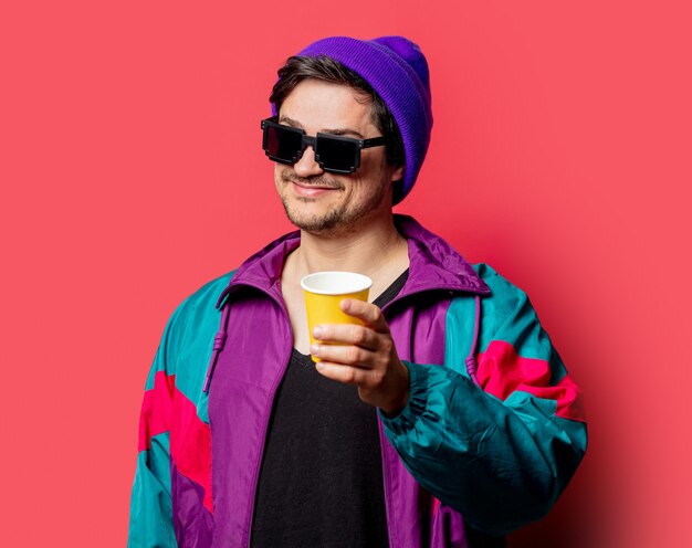 Photo funny guy in 80s style jacket and sunglasses holds paper cup on red backgorund