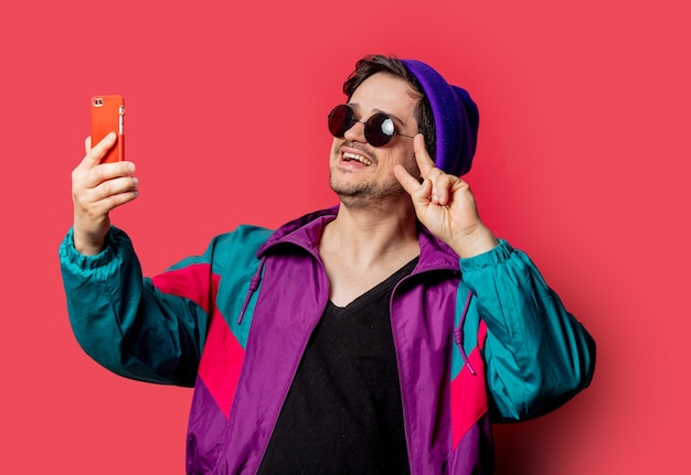 Funny guy in 80s style jacket and sunglasses make selfie on red backgorund