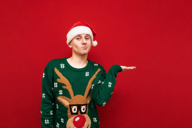 Photo funny guy in christmas clothes stands on a red background looks into the camera