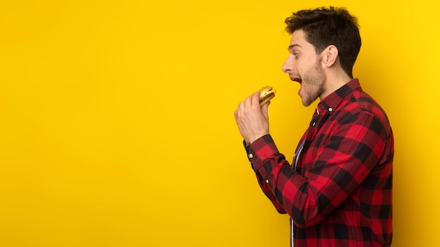 Funny guy holding burger biting sandwich at studio