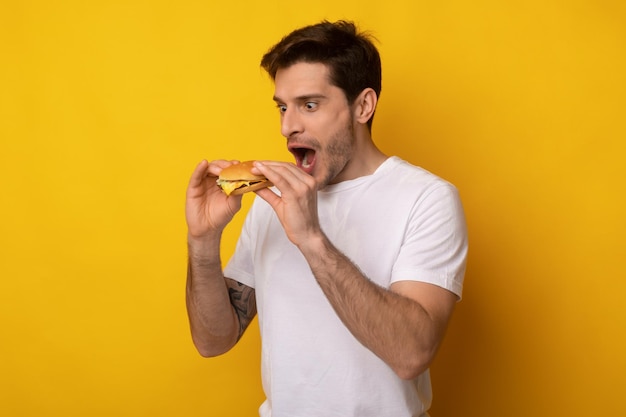 Funny guy holding burger craving sandwich at studio