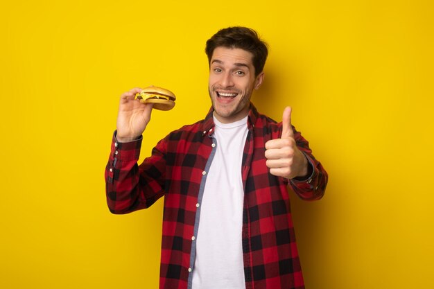 Забавный парень держит бургер, показывая большой палец вверх