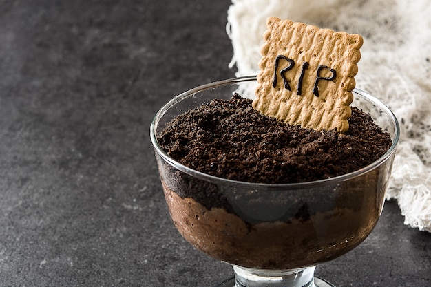 Funny Halloween chocolate mousse with tomb cookie on black stone copy space