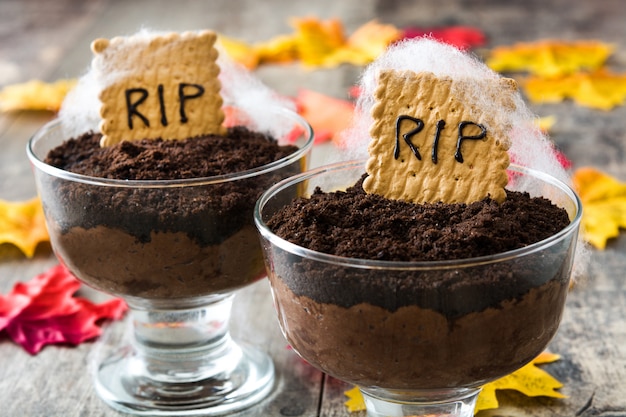 Funny Halloween chocolate mousse with tomb cookie on wooden table