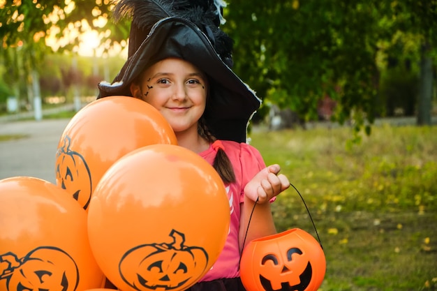 Funny Halloween kid girl with makeup on the face in carnival costumes outdoors.