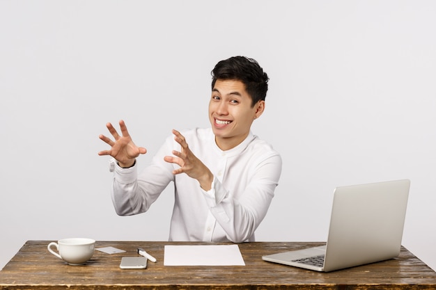 Funny and handsome chinese man in white shirt, catching something as sitting office desk, playing with coworkers during working hours, smiling joyful, fool around