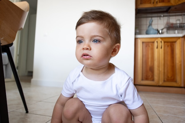 Funny happy healthy toddler sitting at the kitchen at home, pretty eyes, kids play and childhood side view