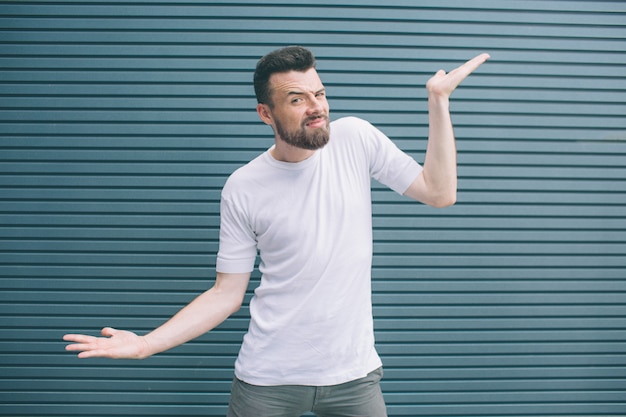 Funny and happy man is standing and posing on camera. One of hands is up and another one is down. Man is smiling. Isolated on striped 