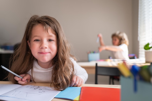 Funny happy schoolgirl writing notes in class. Kids in classroom at school. Pupil at desk in elementary school looking to camera.