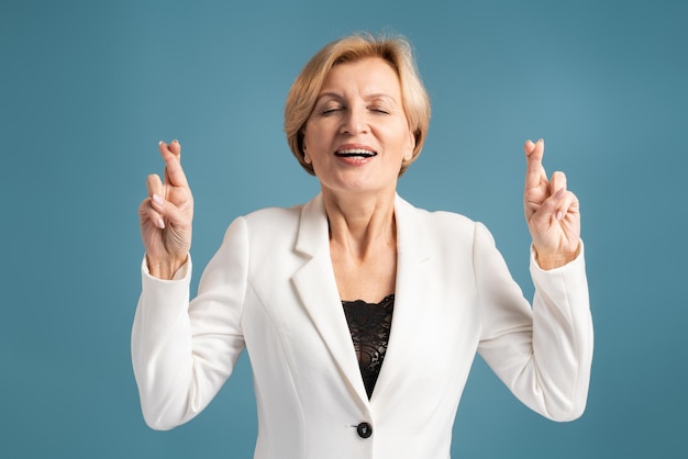 Funny hopeful woman crossing fingers for luck, making a wish, dreaming of innermost, ritual. Indoor studio shot isolated on blue background