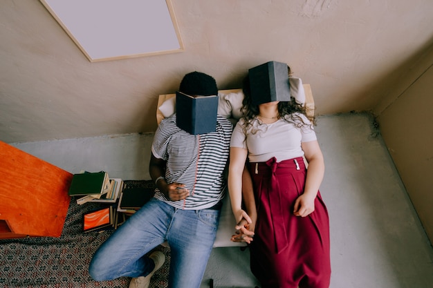 Photo funny interracial couple sitting in chair and sleeping with books on their faces.