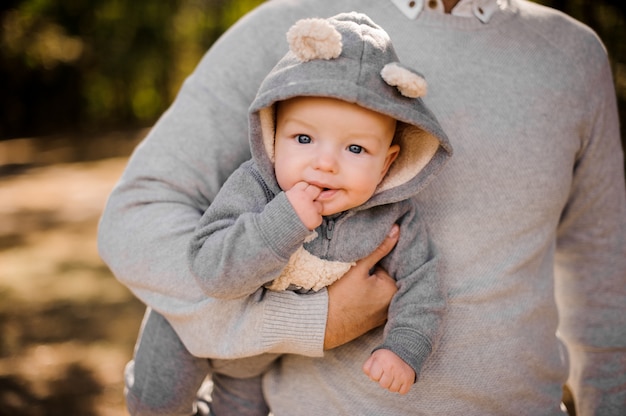 Funny kid bites his fingers in a soft gray suit on the hands of daddy