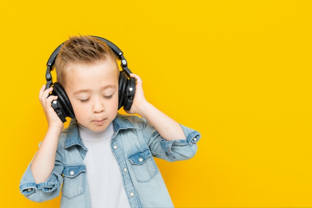 Funny kid in a blue denim shirt listening to music on headphones and enjoying