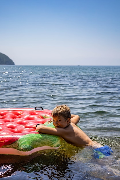 Ragazzo divertente che galleggia su un salvagente di gomma gonfiabile alla fragola circondato da acqua di mare pura e limpida