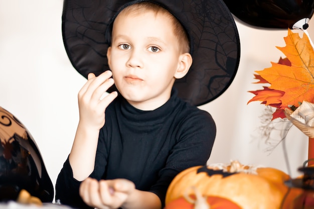 Funny kid boy in witch hat for Halloween party eating candies and have fun.