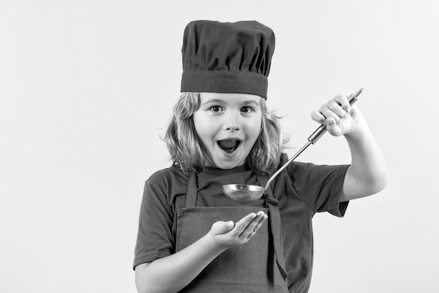 Funny kid chef cook with kitchen ladle studio portrait Cooking children Chef kid boy making healthy food Portrait of little child in chef hat isolated on studio background