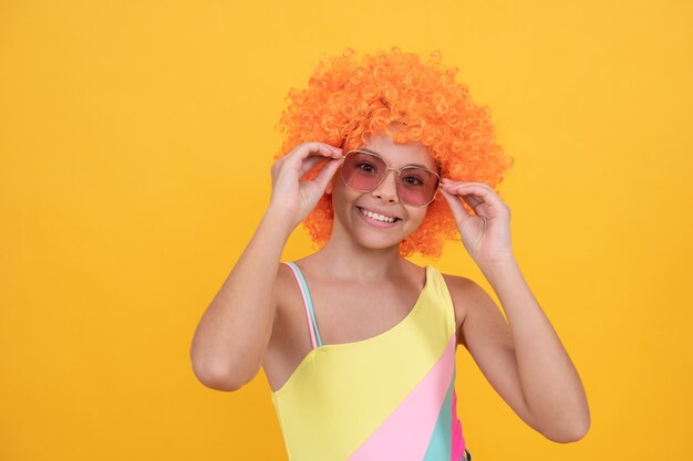 Funny kid in curly clown wig having fun child wear sunglasses and swimsuit