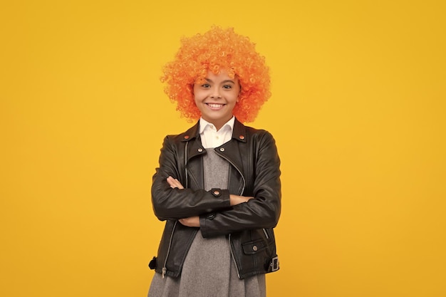 巻き毛の赤毛のかつらで面白い子供 楽しい時を過す ピエロであるオレンジ色の髪の 10 代の少女 幸せな女の子の顔の肯定的で笑顔の感情