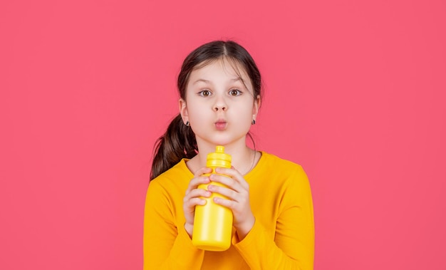 Bambino divertente bere acqua su sfondo rosa