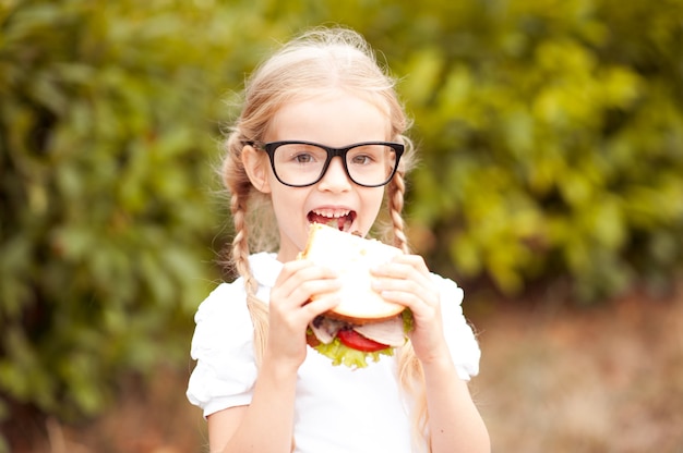 Photo funny kid girl eating sandwich outdoors