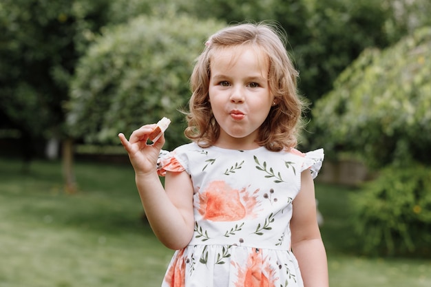 Funny kid girl eating sandwich outdoors.