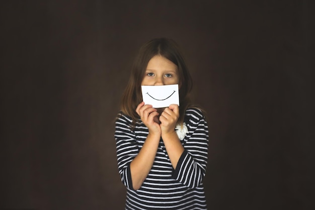 Funny kid girl with cardboard smile concept emotion and childhood