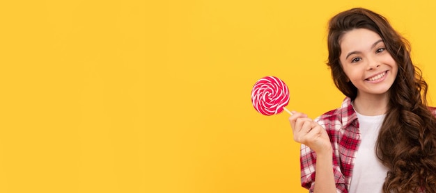 Funny kid hold lollipop caramel candy on yellow background show peace gesture Teenager child with sweets poster banner header copy space