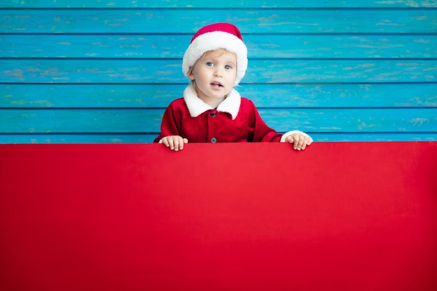 Funny kid holding cardboard banner blank. Child playing at home. Christmas holiday concept. Copy space.