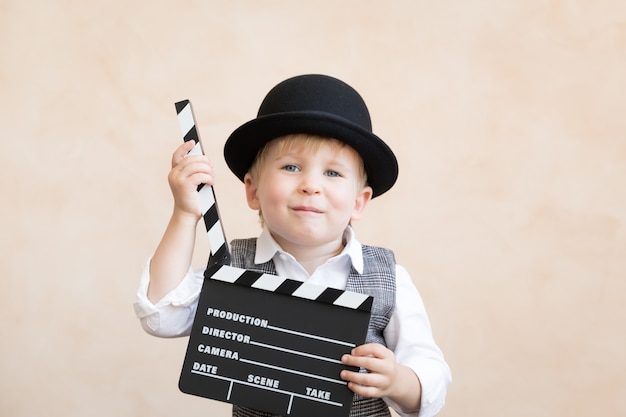 Funny kid holding clapper board. Happy child having fun at home. Retro cinema concept
